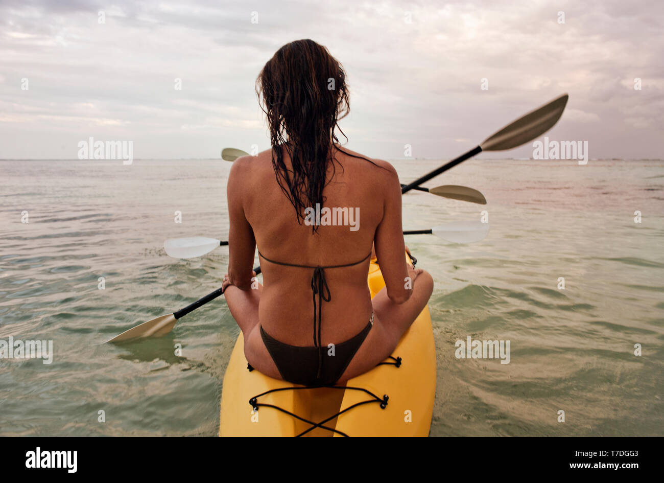 Mid adult woman wearing a bikini while sitting at the end of a sea kayak in the ocean. Stock Photo