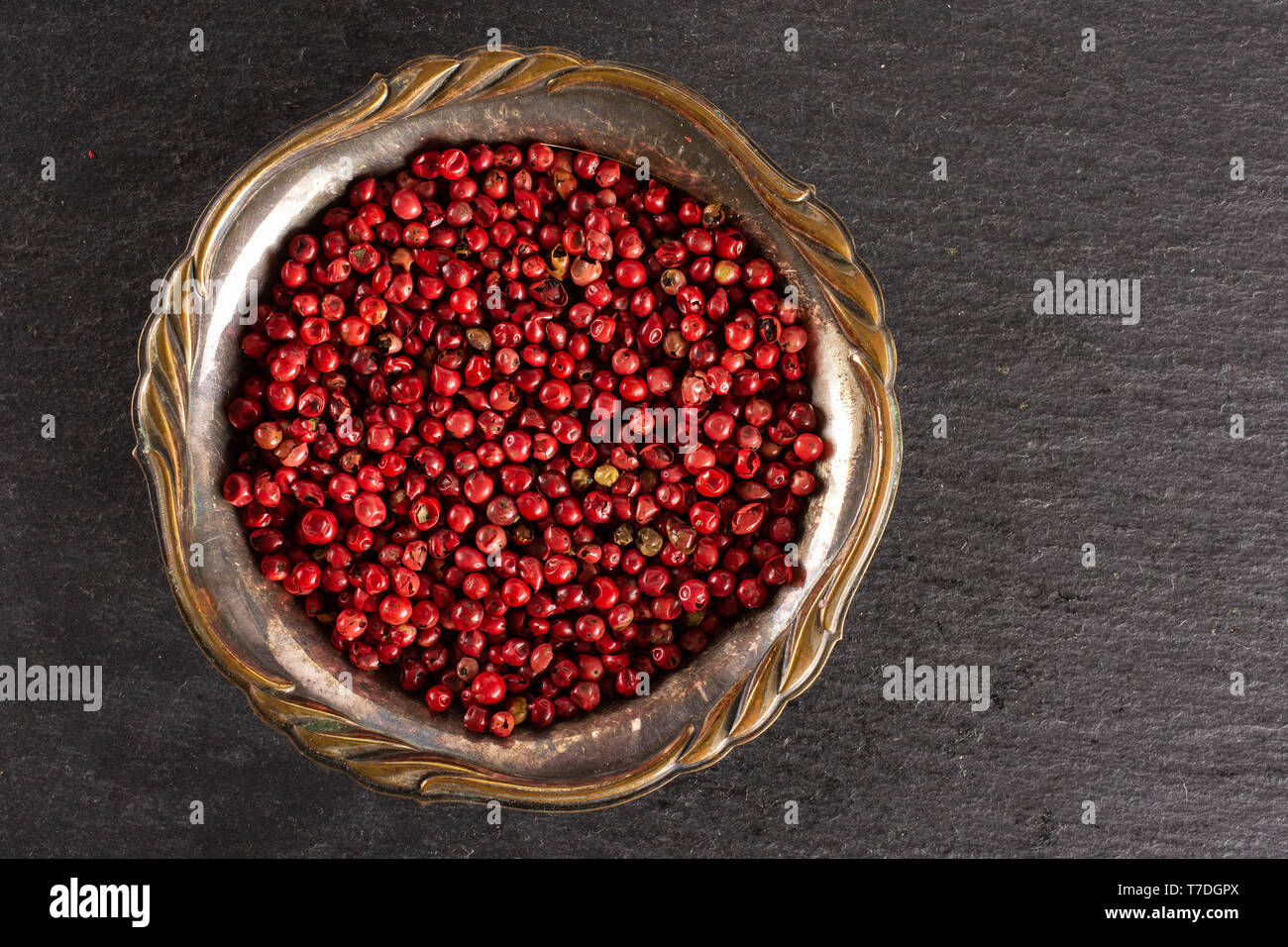 Lot of whole peruvian pink pepper in old iron bowl flatlay on grey stone Stock Photo