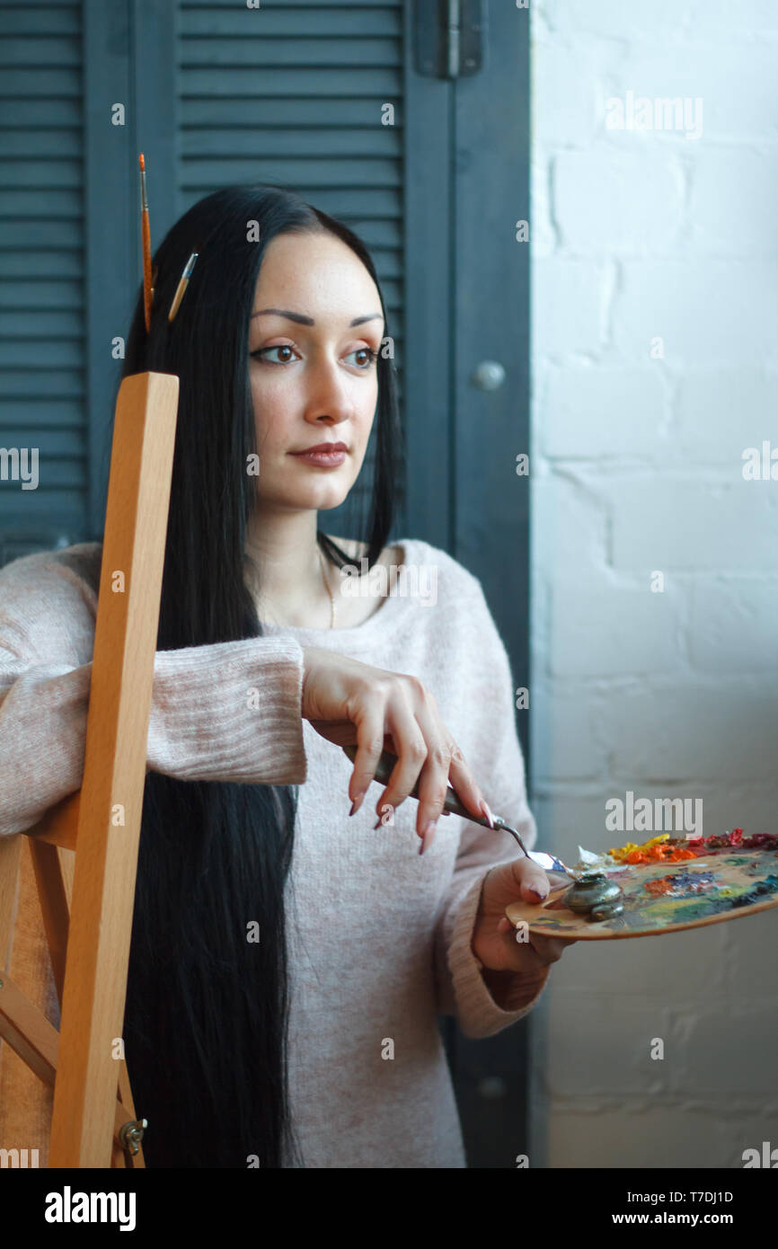 Closeup of a young woman with black hair mixes paint on a palette with a  brush against a white canvas, creating an oil painting, soft focus Stock  Photo - Alamy