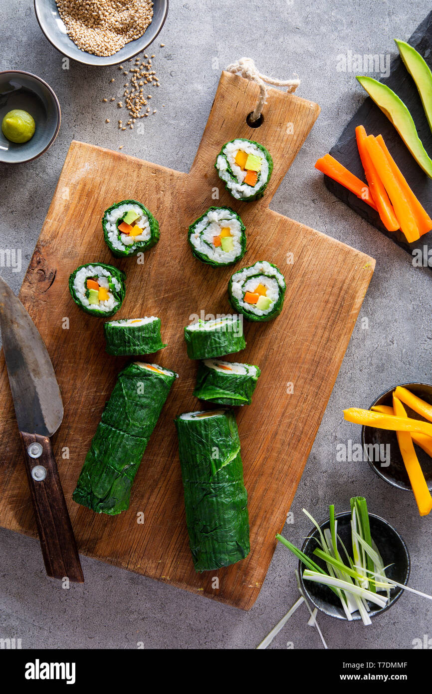 Springlike vegan maki sushi with spinach, avocado, carrots, mango and shallots on wooden board over grey concrete background Stock Photo