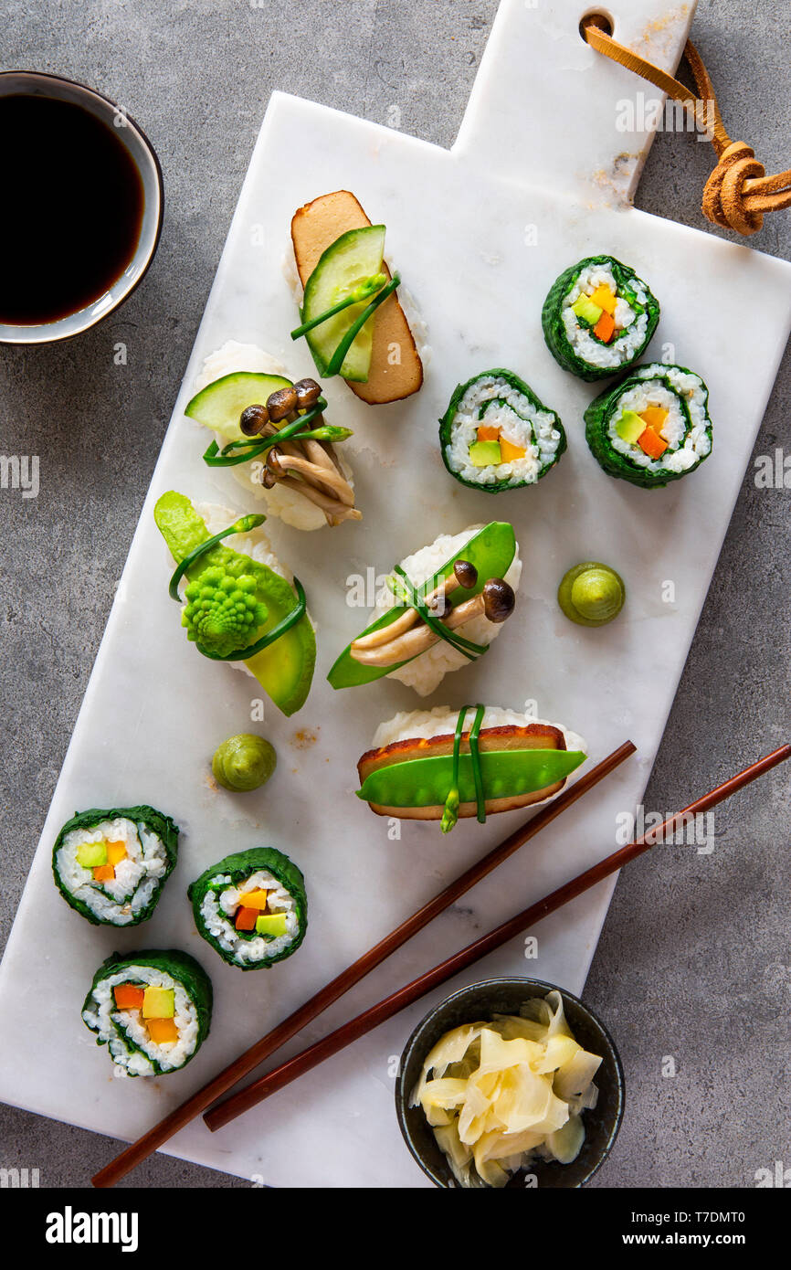 Springlike vegan maki and nigiri sushi with smoked tofu, mushrooms, fresh fruit and vegetables on white marble board over grey concrete background Stock Photo