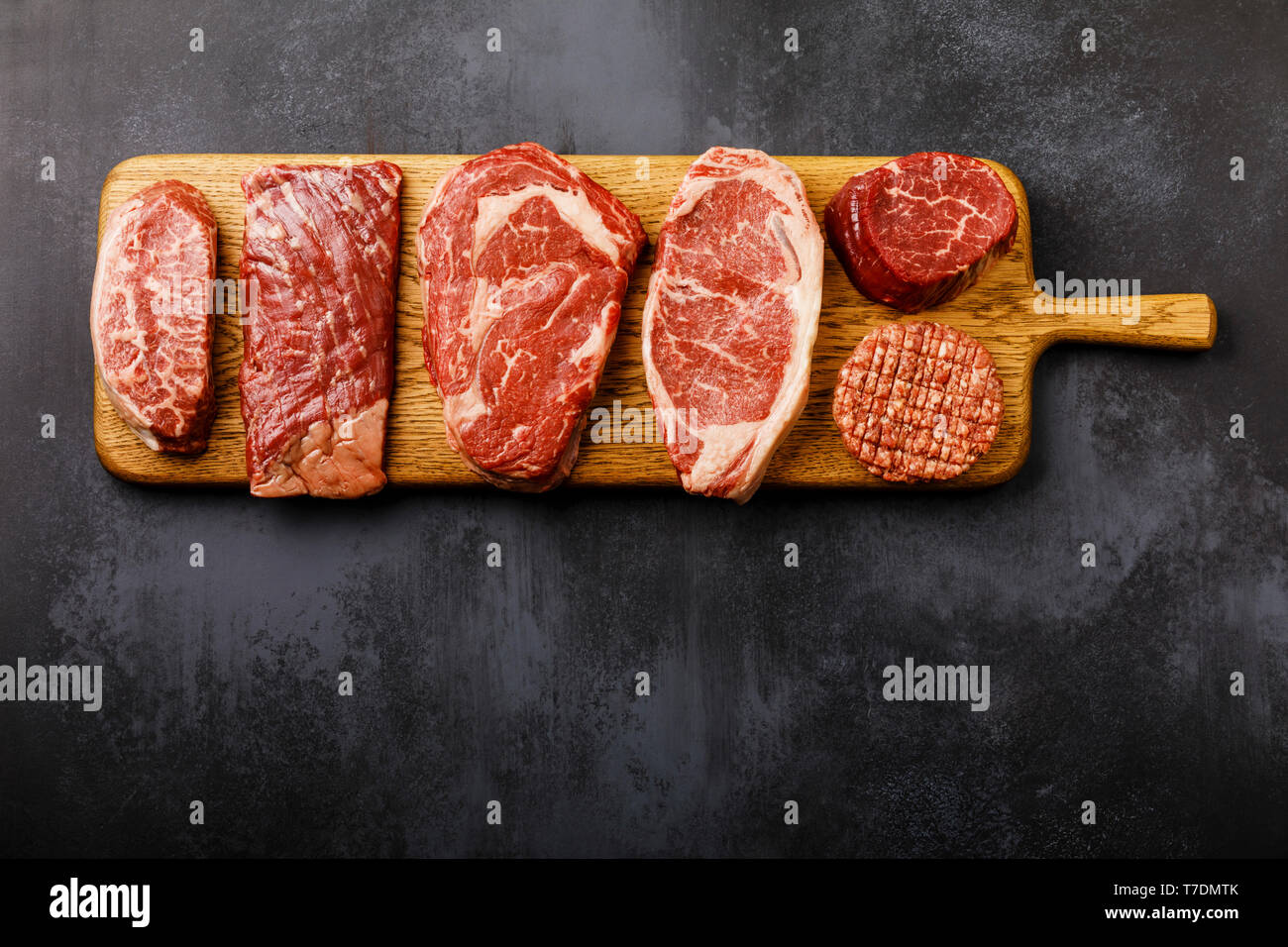 Variety of Raw Black Angus Prime meat steaks Top Blade, Machete, Rib Eye, Striploin, Tenderloin fillet Mignon, Cutlet Burger on wooden board on dark b Stock Photo