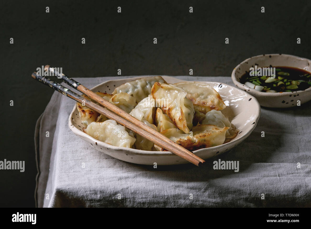 Fried asian dumplings Gyozas potstickers in white ceramic plate served with chopsticks and bowl of soy onion sauce over linen table cloth. Asian dinne Stock Photo