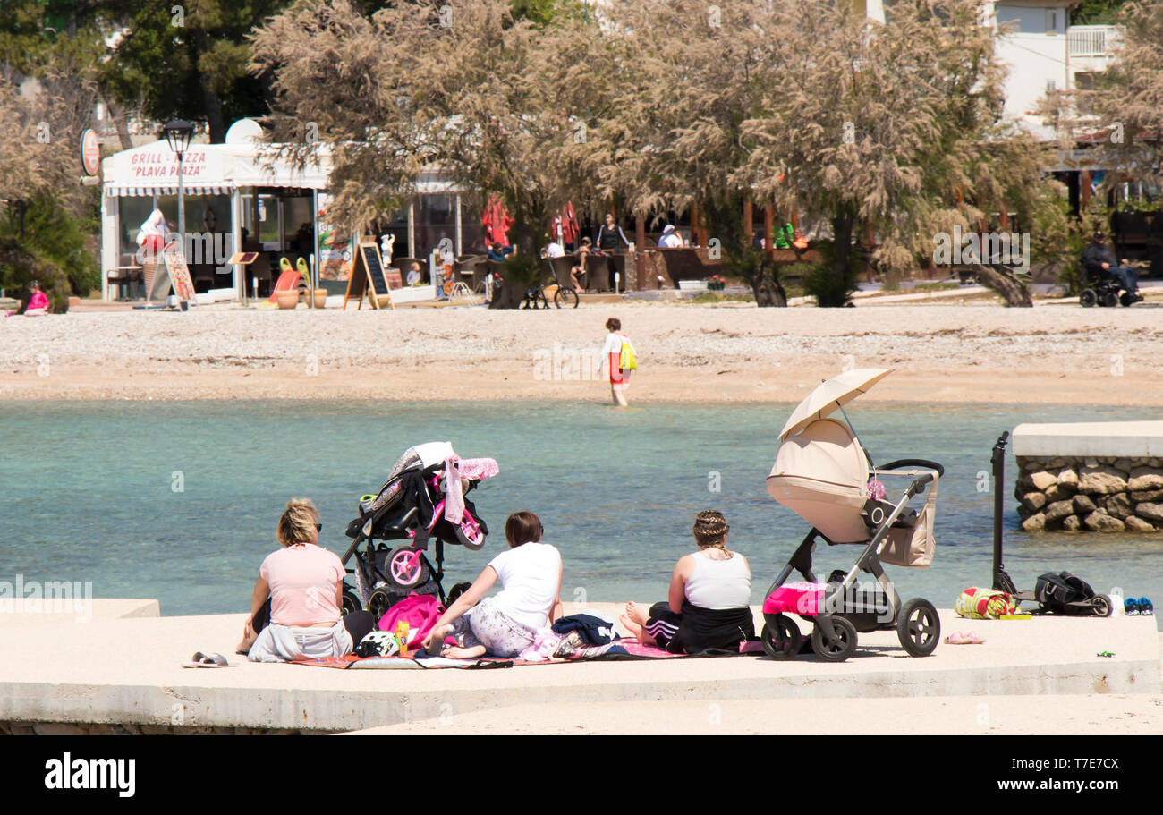 Vodice, Croatia - May2, 2019: Group of mothers sitting on the beach in spring off-season with baby strollers next to them Stock Photo