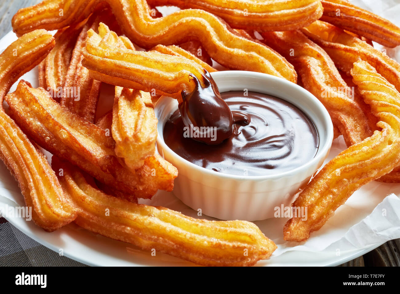 delicious deep fried churros served with chocolate dipping on a white plate on a wooden table with napkin, Traditional spanish and mexican street food Stock Photo