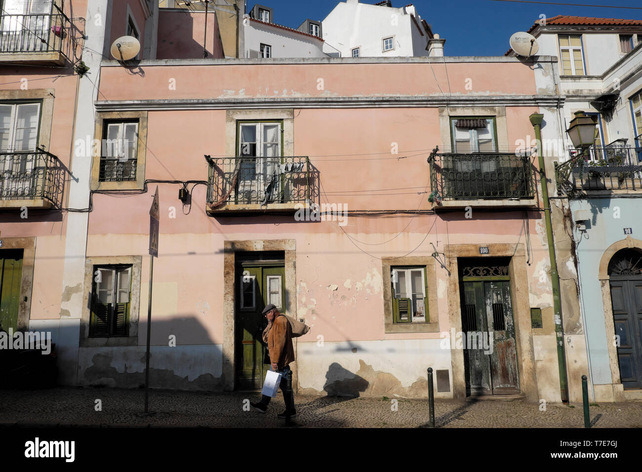 Old man carrying hessian sack and food bag walking past a house on a street in the Alfama district of Lisbon Portugal Europe EU  KATHY DEWITT Stock Photo