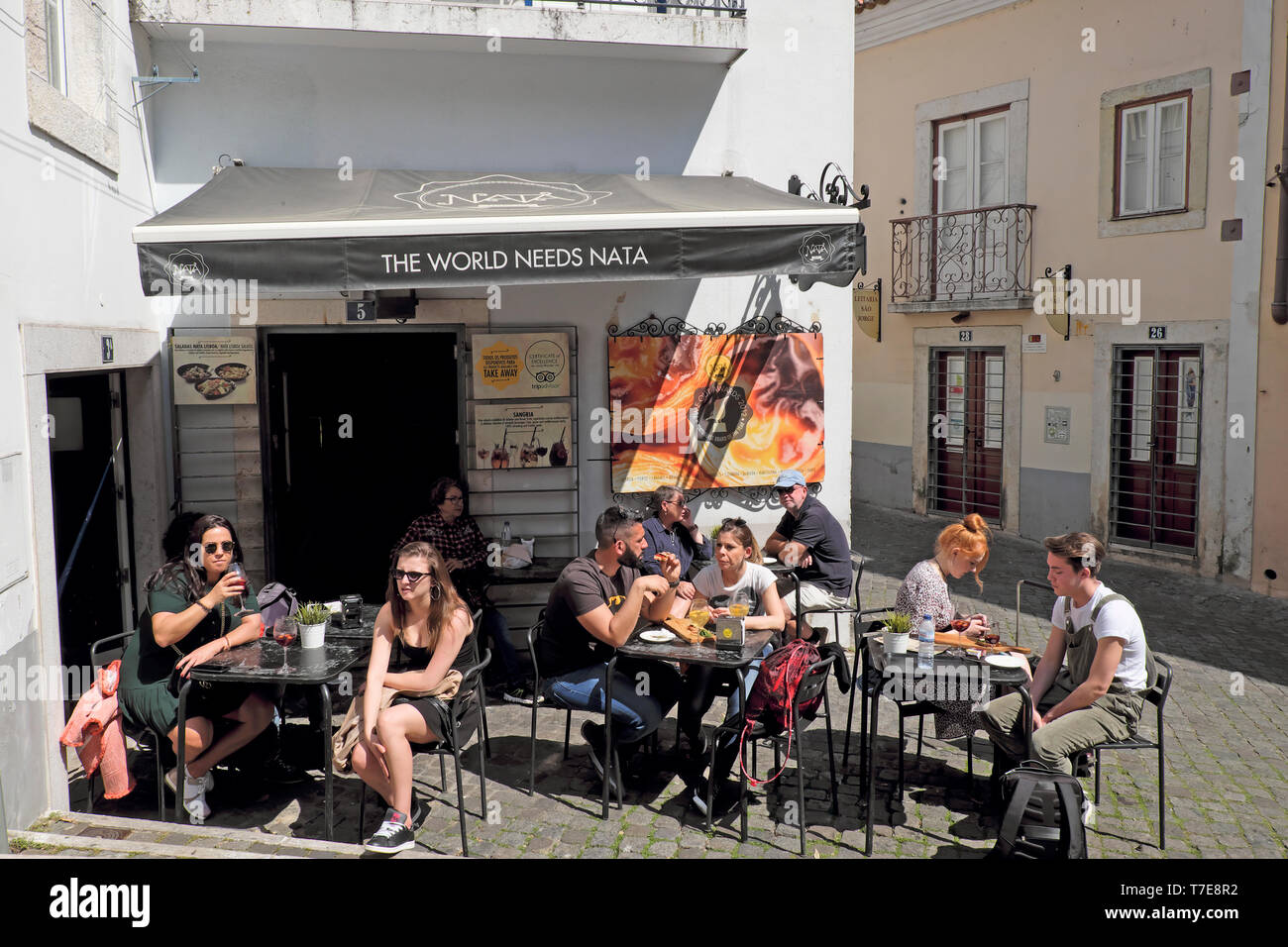Tourists customers sitting eating and drinking outside at 'The World Needs Nata' cafe selling pastel de nata Portuguese custard tarts Lisbon Portugal Stock Photo