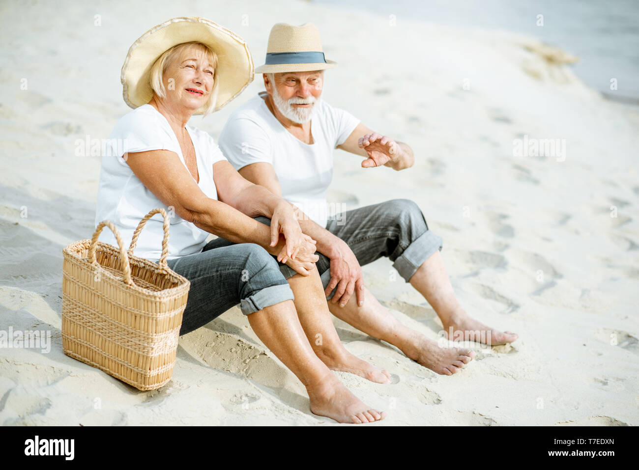 Lovely senior couple relaxing, sitting together on the sandy beach ...