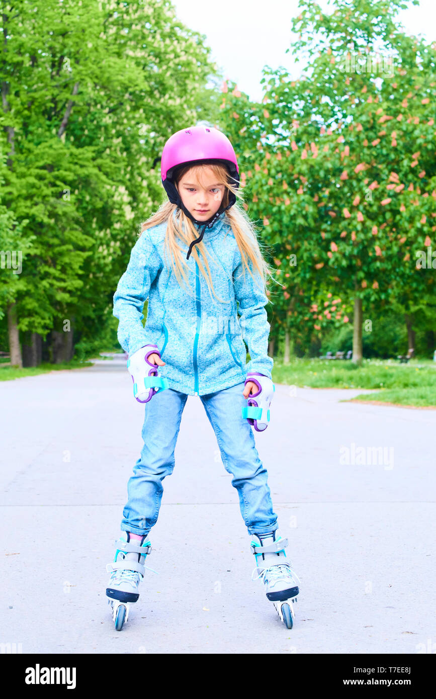 Cute little child girl learning to roller skate on beautiful summer day