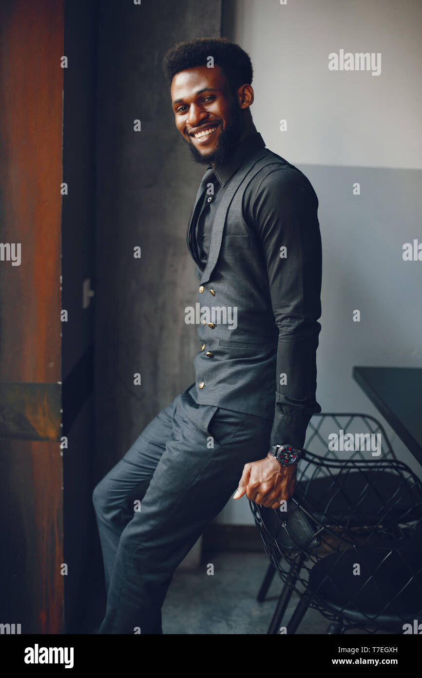 A young and handsome dark-skinned boy in a black suit standing in a cafe Stock Photo