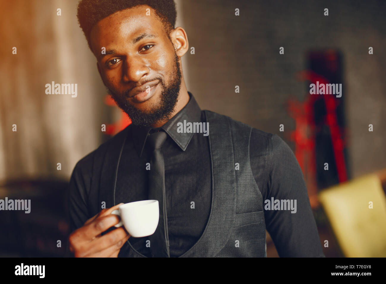 A young and handsome dark-skinned boy in a black suit standing in a cafe Stock Photo