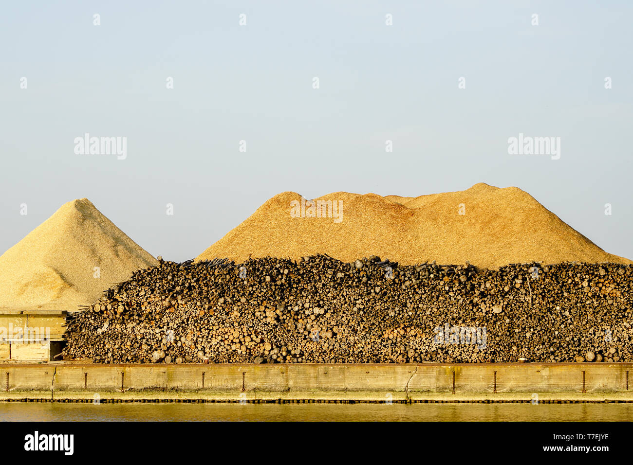 Big piles of wooden logs and wood chips under blue sky in the harbor ...