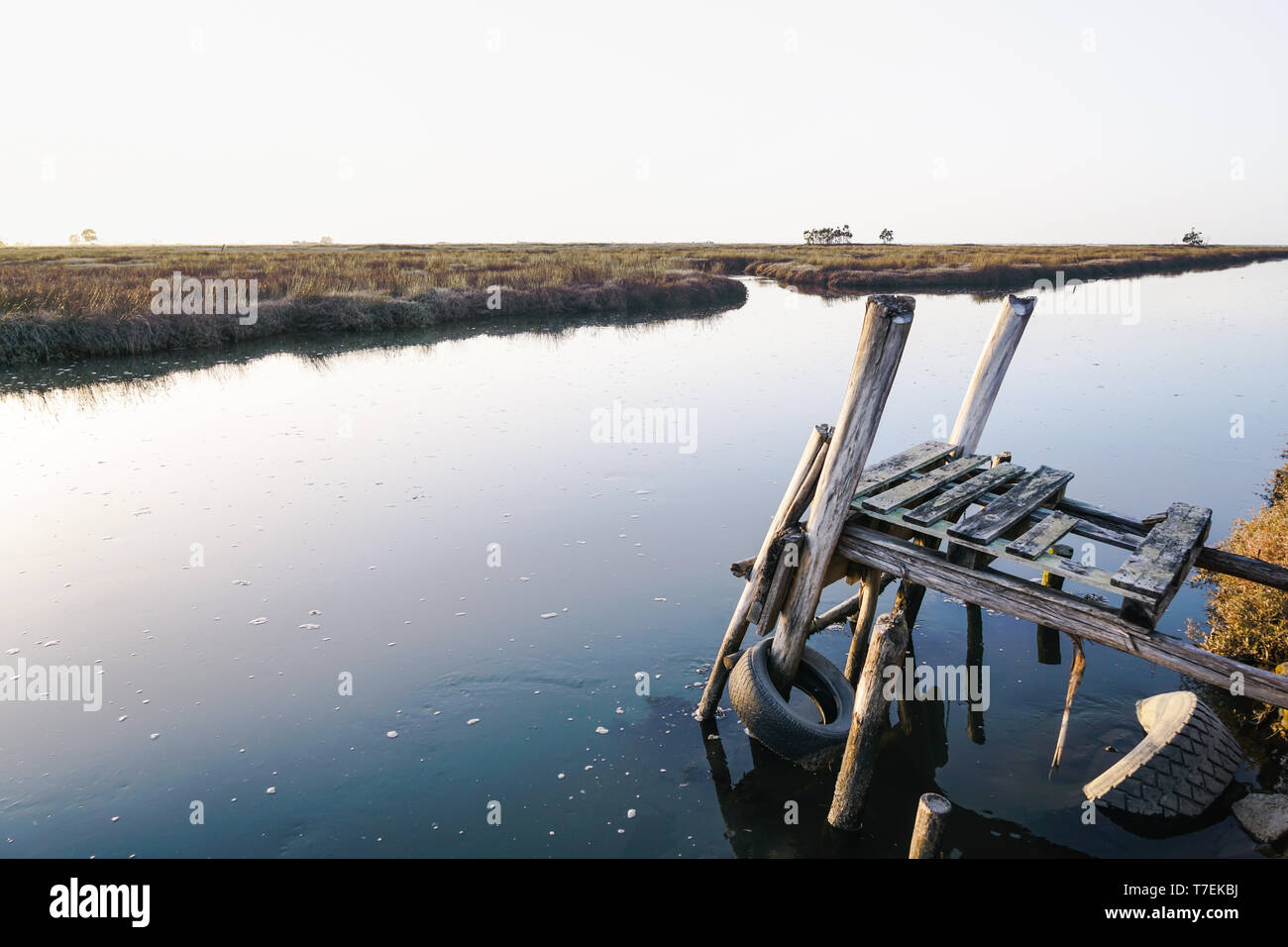 Weathered and rickety wooden dock almost collapsing in the Aveiro lagoon. Beautiful view of the water in bright day. Stock Photo