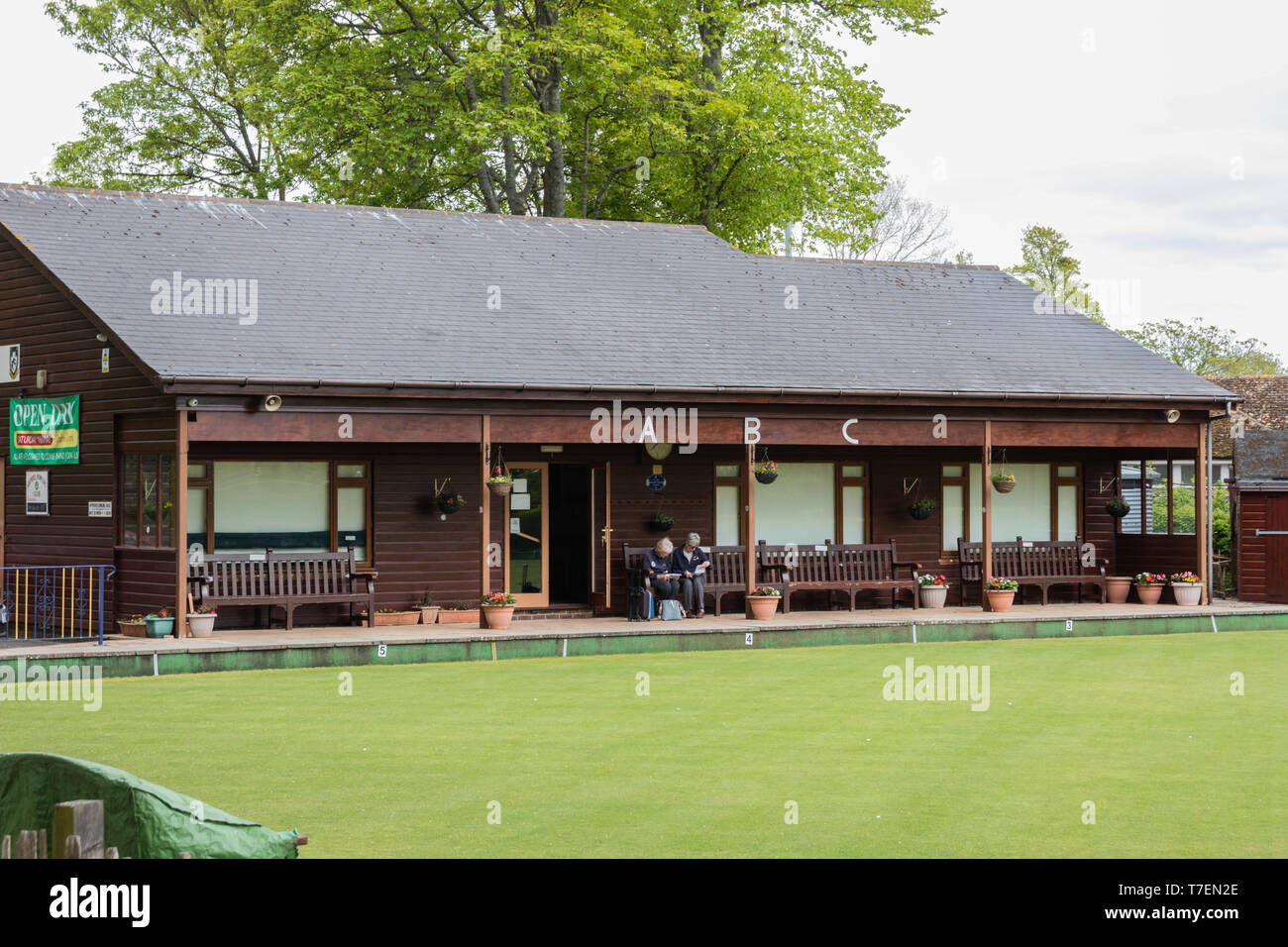 A pair of elderly women sat in the pavilion of a green bowling club with perfect bowling lawn in the foreground Stock Photo