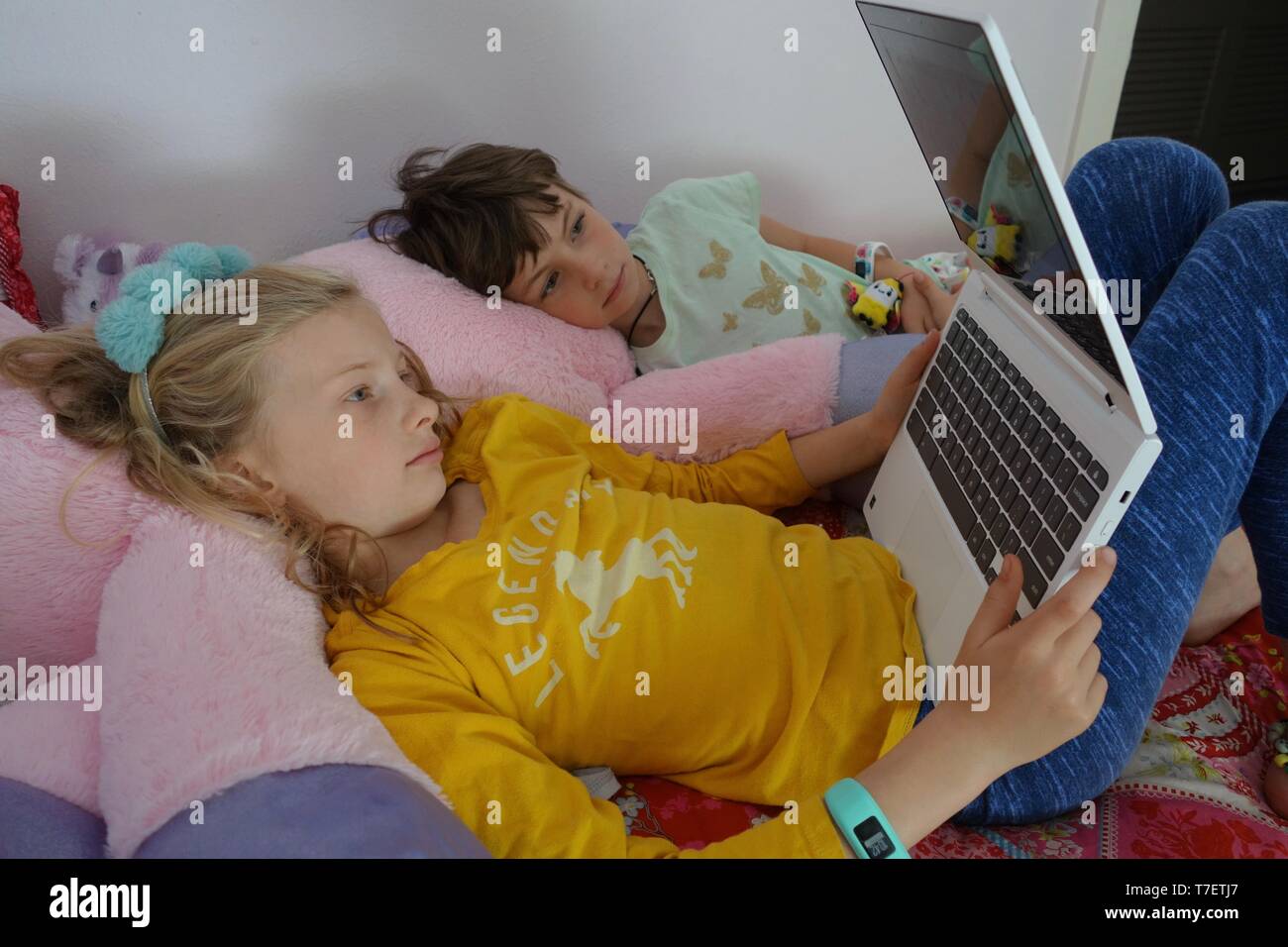 Two young girls laying on bed watching internet videos on a laptop Stock Photo