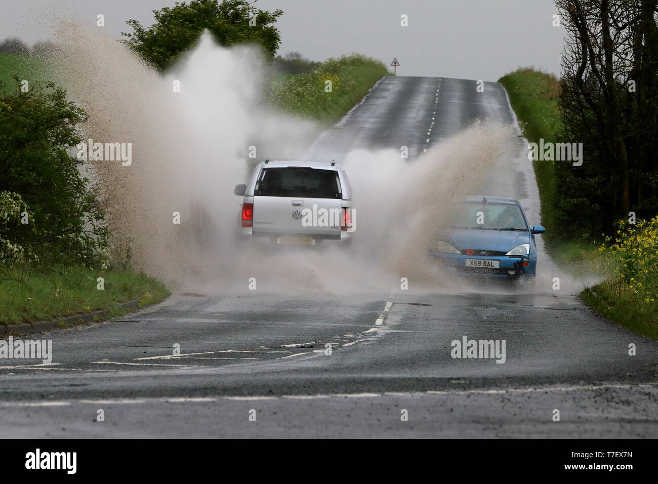 SUV splashing on coming car as it goes through a large puddle of standing water Stock Photo