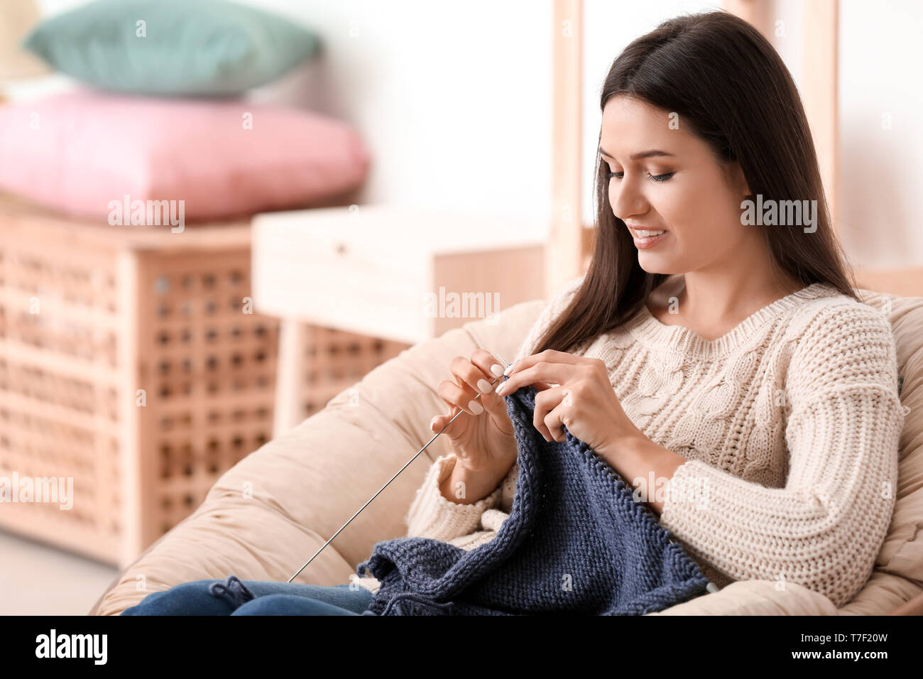 Young woman sitting in armchair and knitting warm sweater indoors Stock ...
