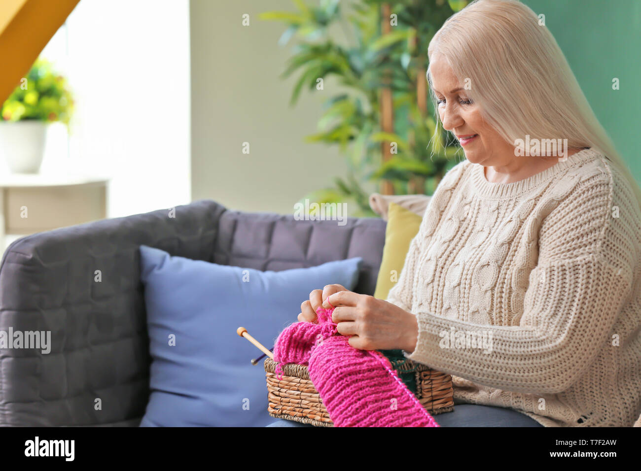 Mature woman sitting on sofa and knitting warm sweater indoors Stock ...