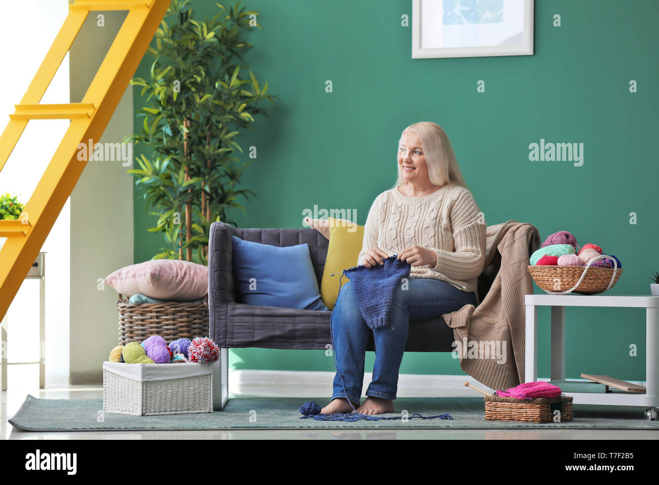 Mature woman sitting on sofa and knitting warm sweater indoors Stock ...