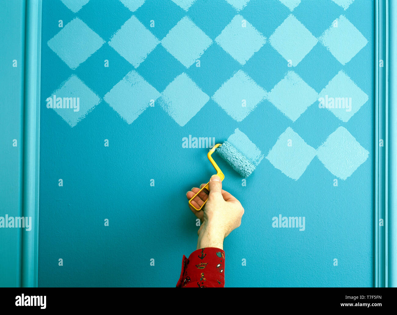 Hand using roller to paint chequerboard pattern on wall Stock Photo