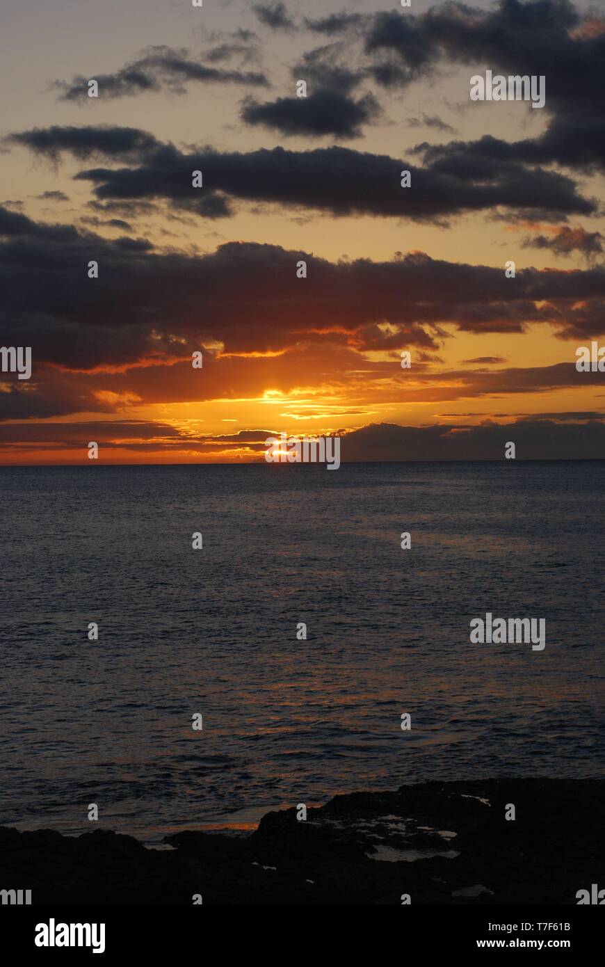 Sun setting over the ocean in Oahu Hawaii, Hawaiian island sunset orange glowing sky with clouds portrait orientation Stock Photo