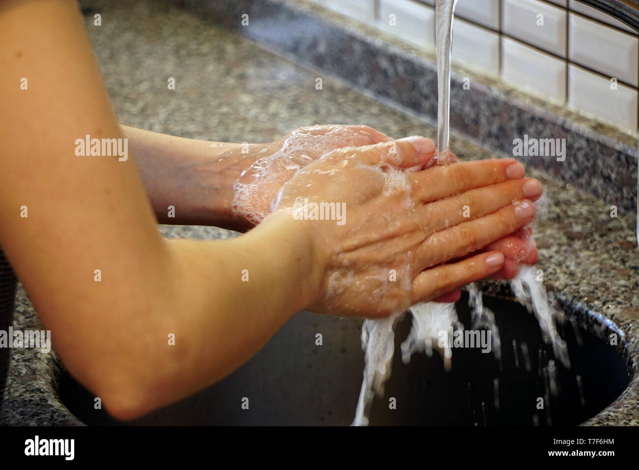 Woman washing hands with water and soap under the water in the kitchen ...