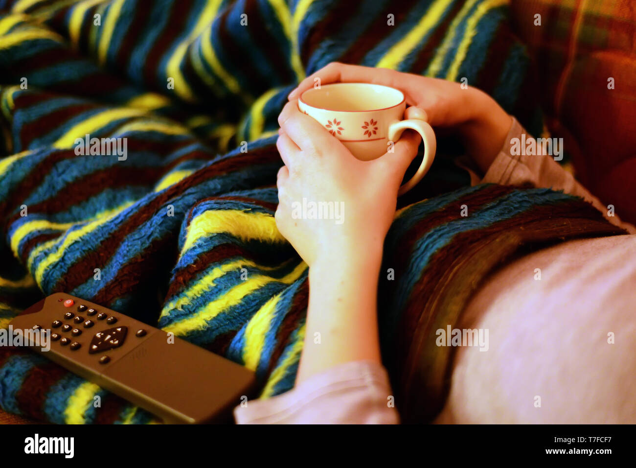 Chilling at home under the blanket with remote control and tea mug in hand Stock Photo
