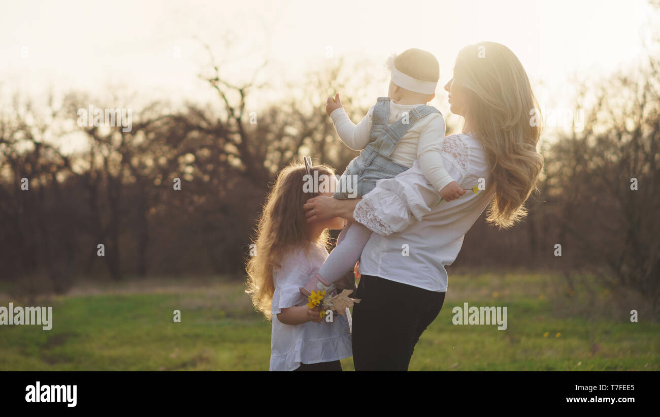 Single mother with two daughters in the rays of sunset. Walk on mother's day. Back view. Family bonding concept. Carefree. Happy childhood. Man is unr Stock Photo