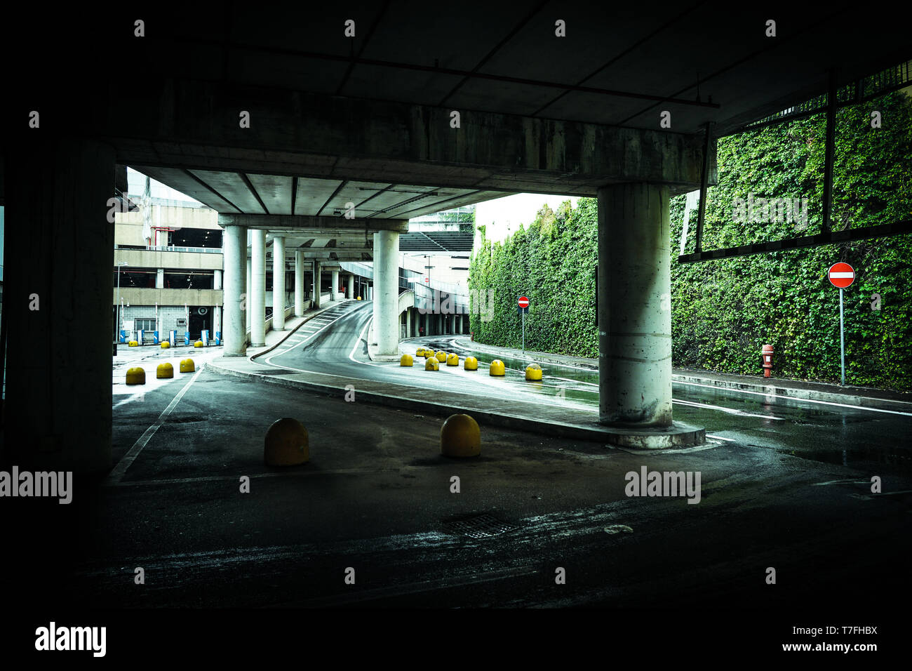 Full lenght of modern car parking entry path with concrete columns and asphalt road dark rainy day Stock Photo