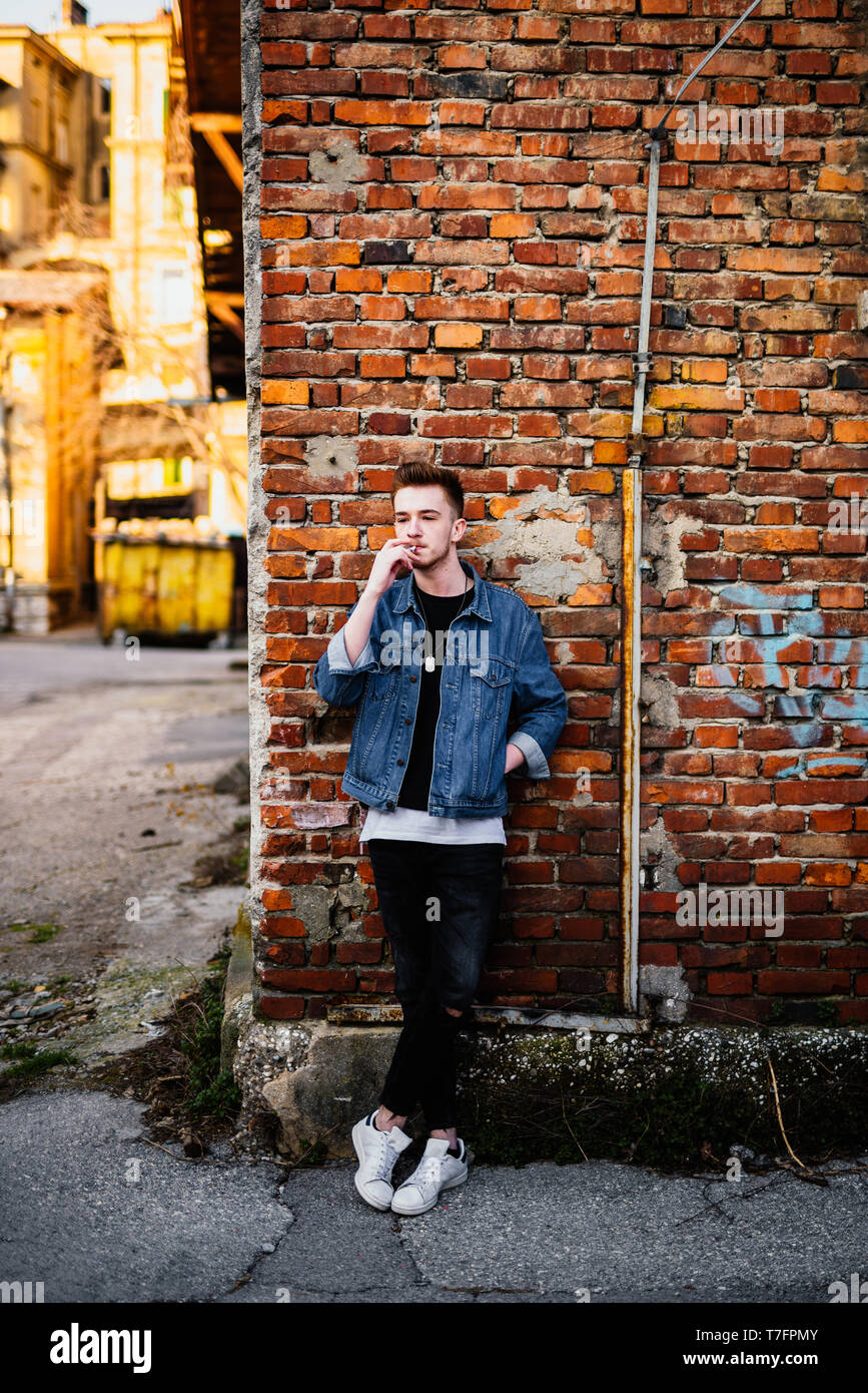 Young man in front of brick wall smoking cigarette Stock Photo