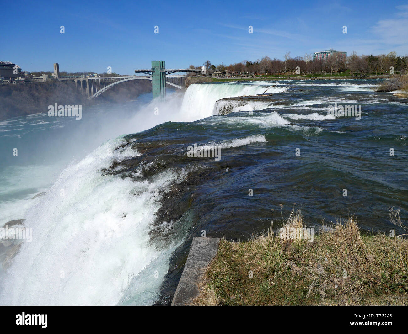 Niagara Falls, close up view of the edge of the waterfall with Rainbow Bridge and observation tower in the background Stock Photo