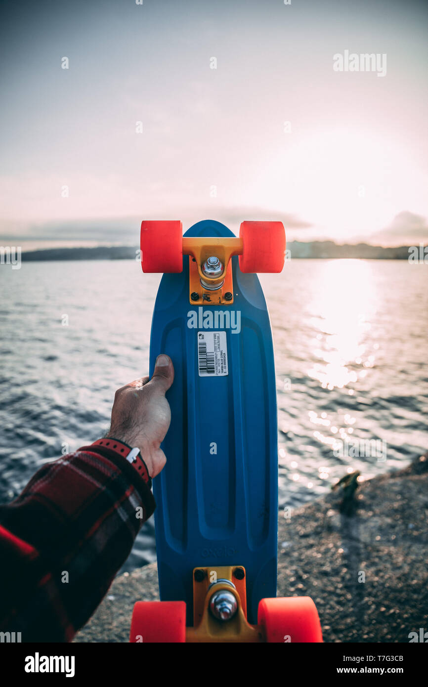 Handhold Colorful skateboard in front of the ocean at sunset Stock Photo