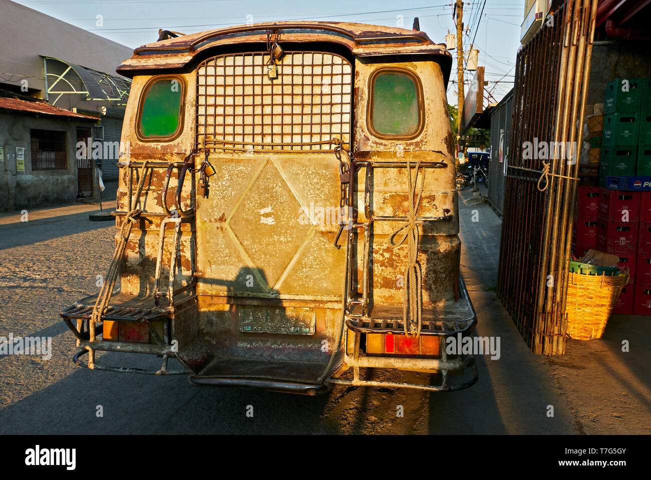 Rear of an old rusty jeepney type of delivery truck, with green windows several padlocks attached to it, parking in the streets of Iloilo, Philippines Stock Photo