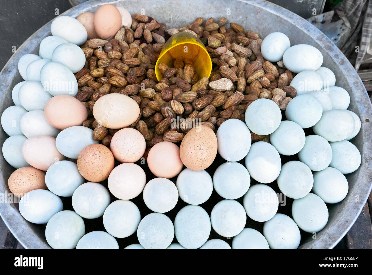 Close-up of steamed peanuts and white and brown boiled eggs, all nicely presented in a metal bowl with a measuring cup, for sale in the street Stock Photo