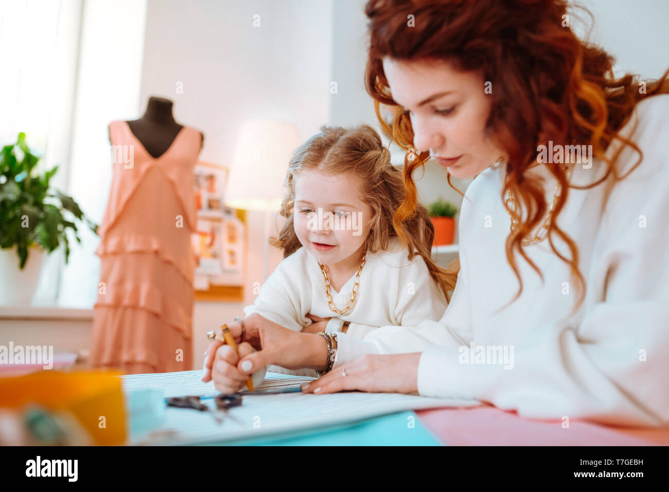 Appealing cute girl standing near mother designing dresses Stock Photo