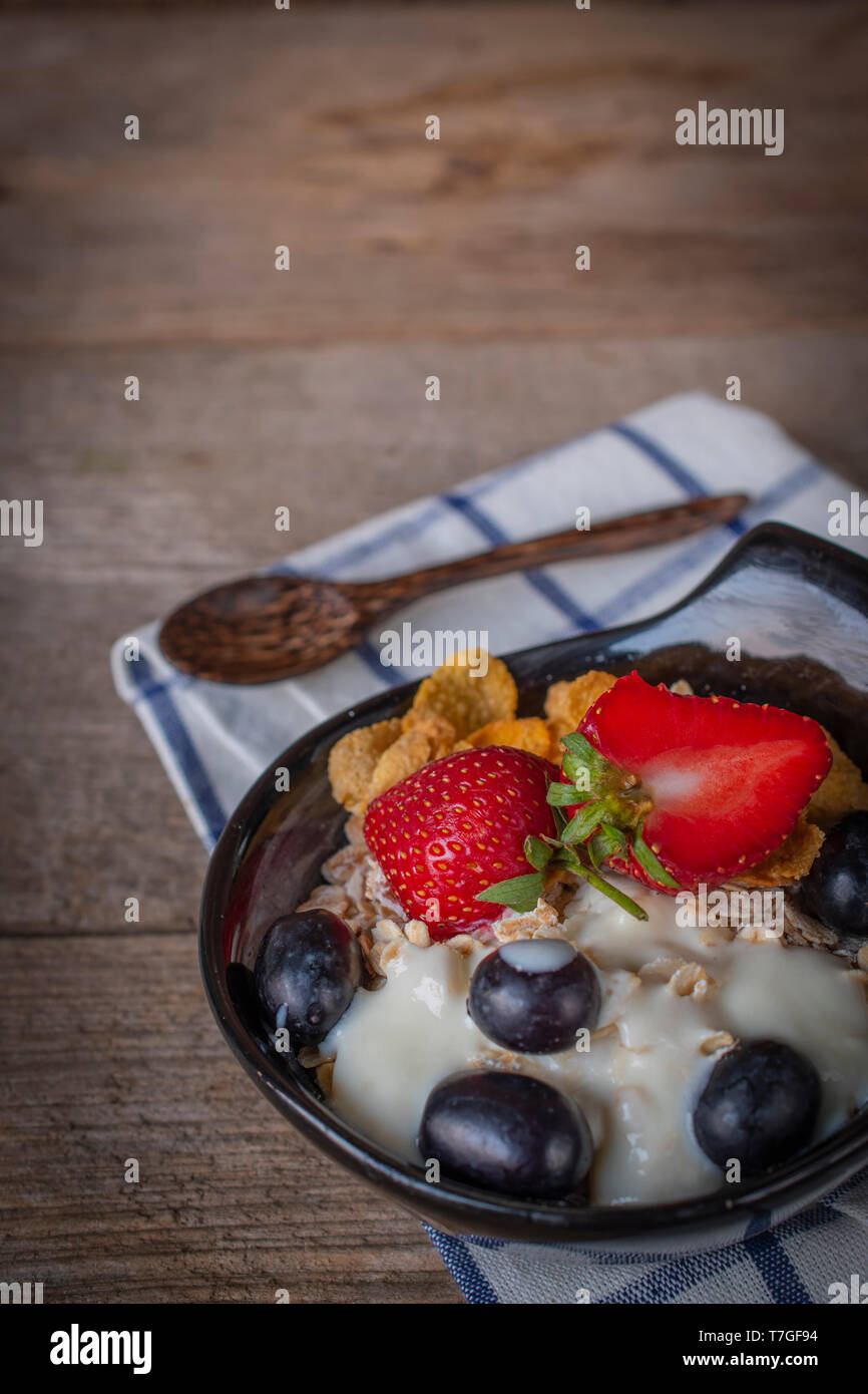 Yoghurt mix oatmeal, strawberry and grape topping in black bowl on Blue and white striped fabric