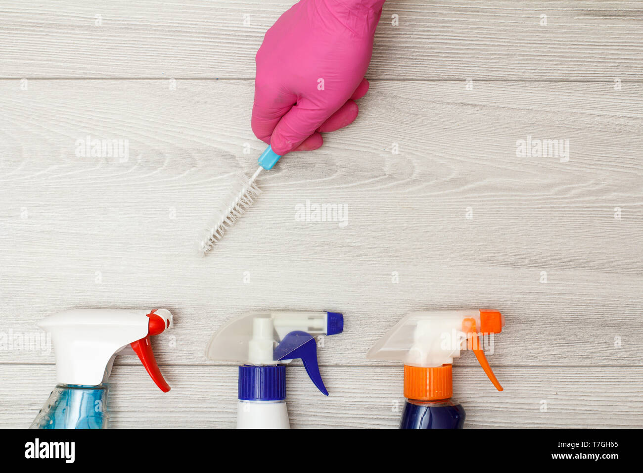 Hand in pink rubber glove holding dust brush with bottles of detergent ...