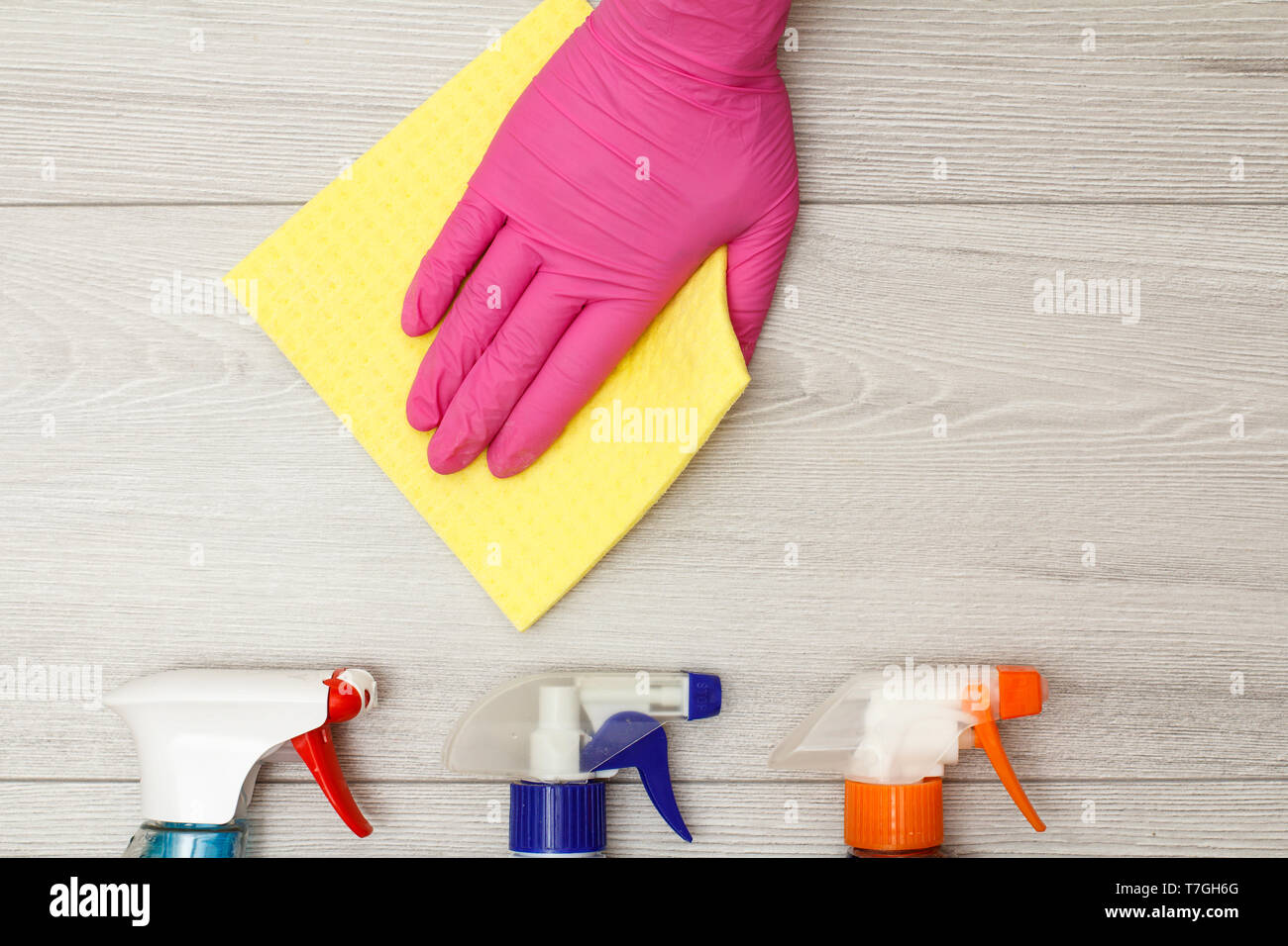 Hand in rubber glove holding yellow napkin with bottles of detergent on ...