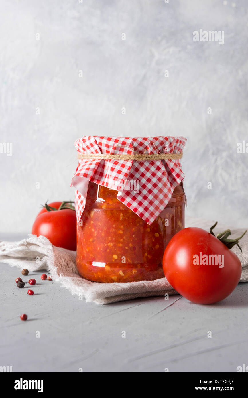 Homemade vegetable sauce adjika with tomatoes in jar on light background. Close-up. Space for text. Stock Photo