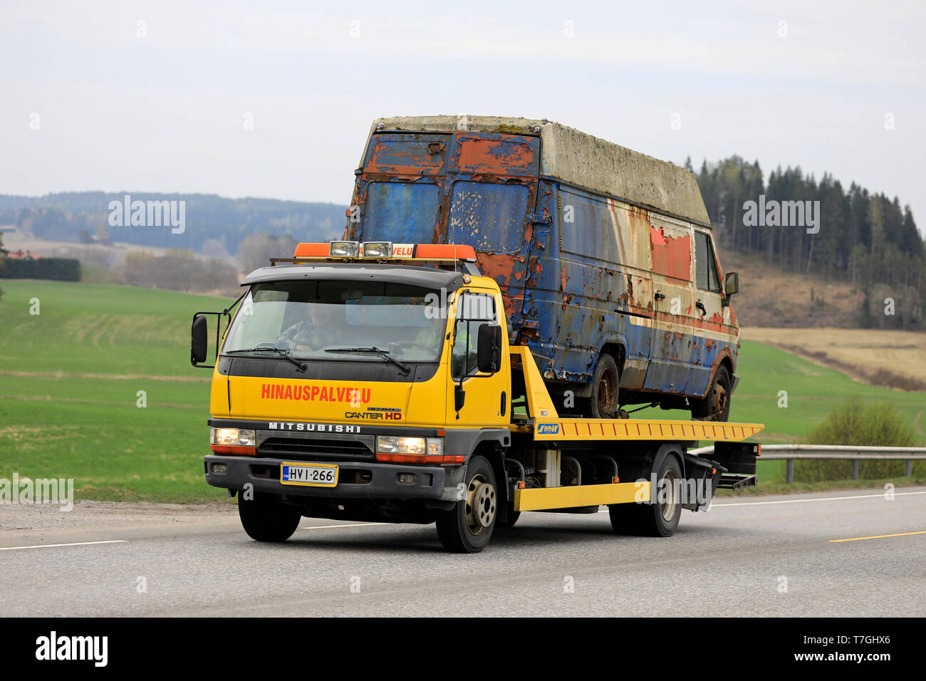 Salo, Finland - April 26, 2019: Yellow Mitsubishi Fuso Canter tow truck carries an old breakdown van along highway on a day of spring. Stock Photo