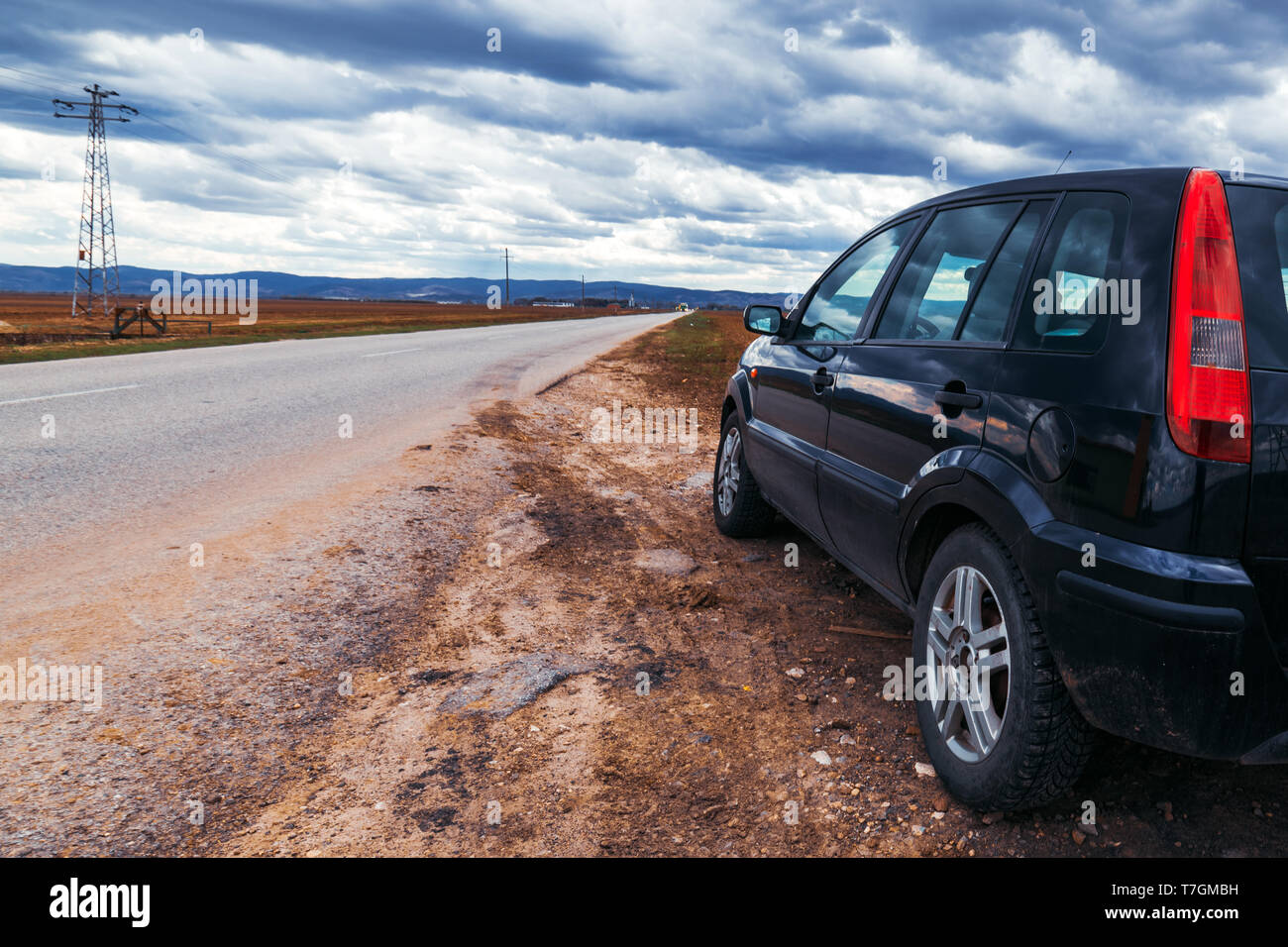 Broken car stopped by the road on stormy day, dramatic clouds on the sky Stock Photo