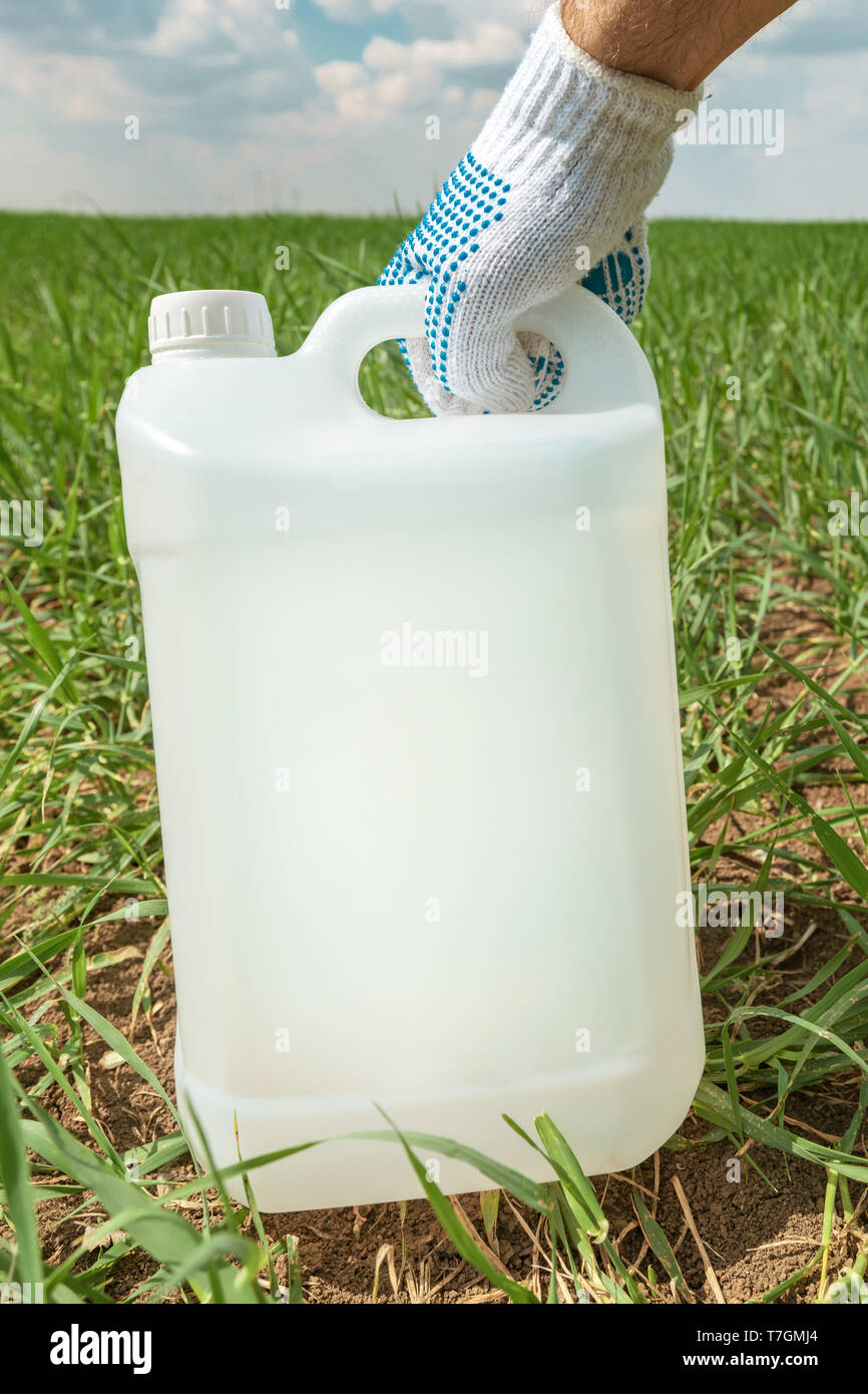 Farmer holding insecticide jug in wheatgrass field, blank plastic container for pesticide chemical as mock up Stock Photo