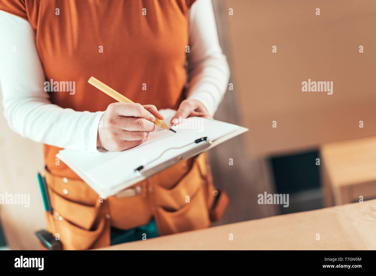 Self employed female carpenter writing project notes on clipboard notepad paper in small business woodwork workshop Stock Photo