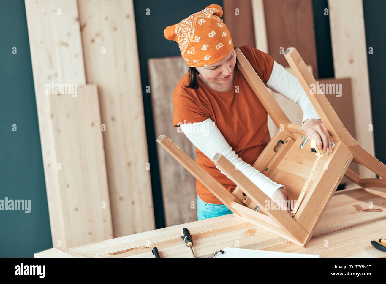 Female carpenter repairing wooden chair seat in small business woodwork workshop Stock Photo