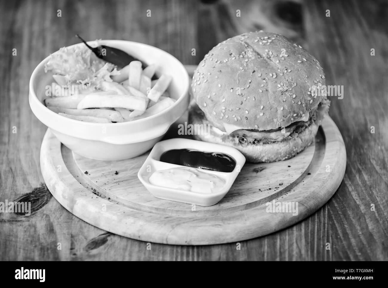 Delicious burger with sesame seeds. Burger menu. High calorie snack. Hamburger and french fries and tomato sauce on wooden board. Fast food concept. Burger with cheese meat and salad. Cheat meal. Stock Photo