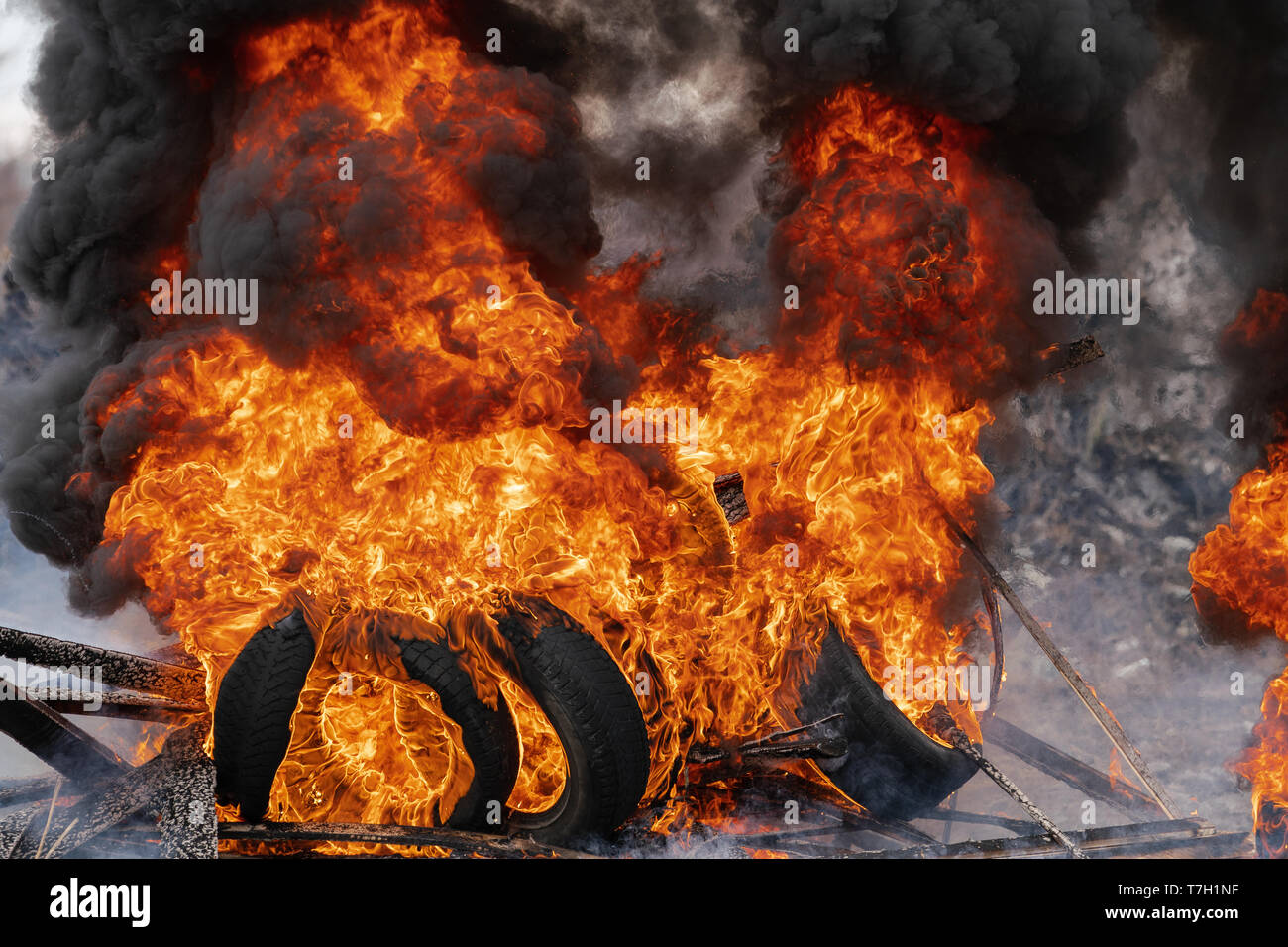 Burning automobile tires, strong flame of red fire and clouds of black smoke in sky. Selective focus, blur from strong fire. Stock Photo