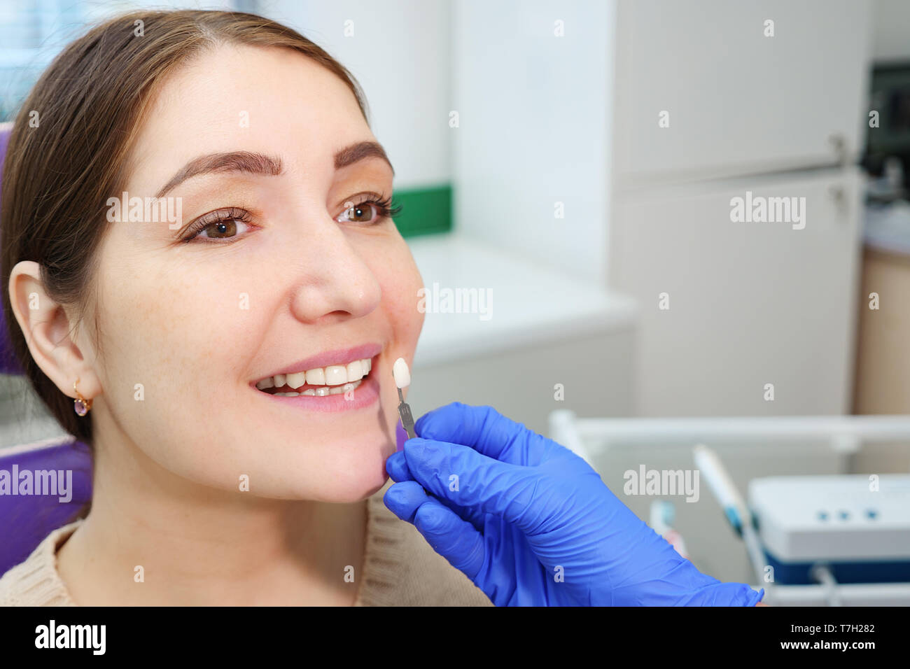 Dentist with tooth color samples is choosing shade for women patient