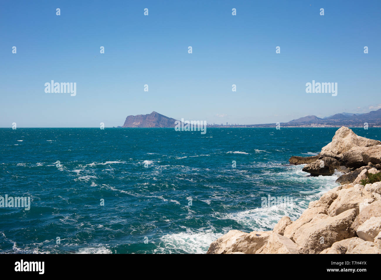 Detail of beach with turquoise and blue sea with Altea and Benidorm in background. Stock Photo