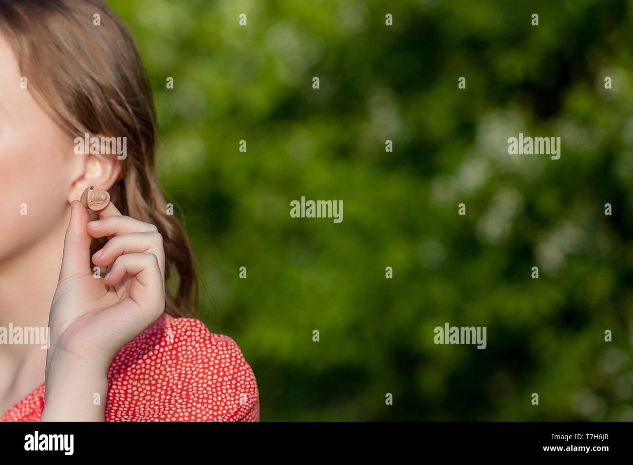 Close-up Of Female Hands Putting Hearing Aid In Ear. Modern digital in the ear hearing aid for deafness and the hard of hearing patients. Stock Photo