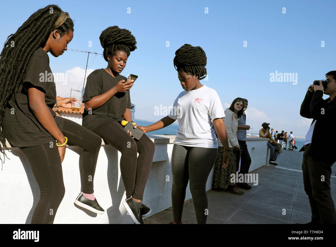 Young women friends tourists teens African hairstyles & woman looking at mobile phone in the Alfama district of Lisbon Portugal Europe KATHY DEWITT Stock Photo